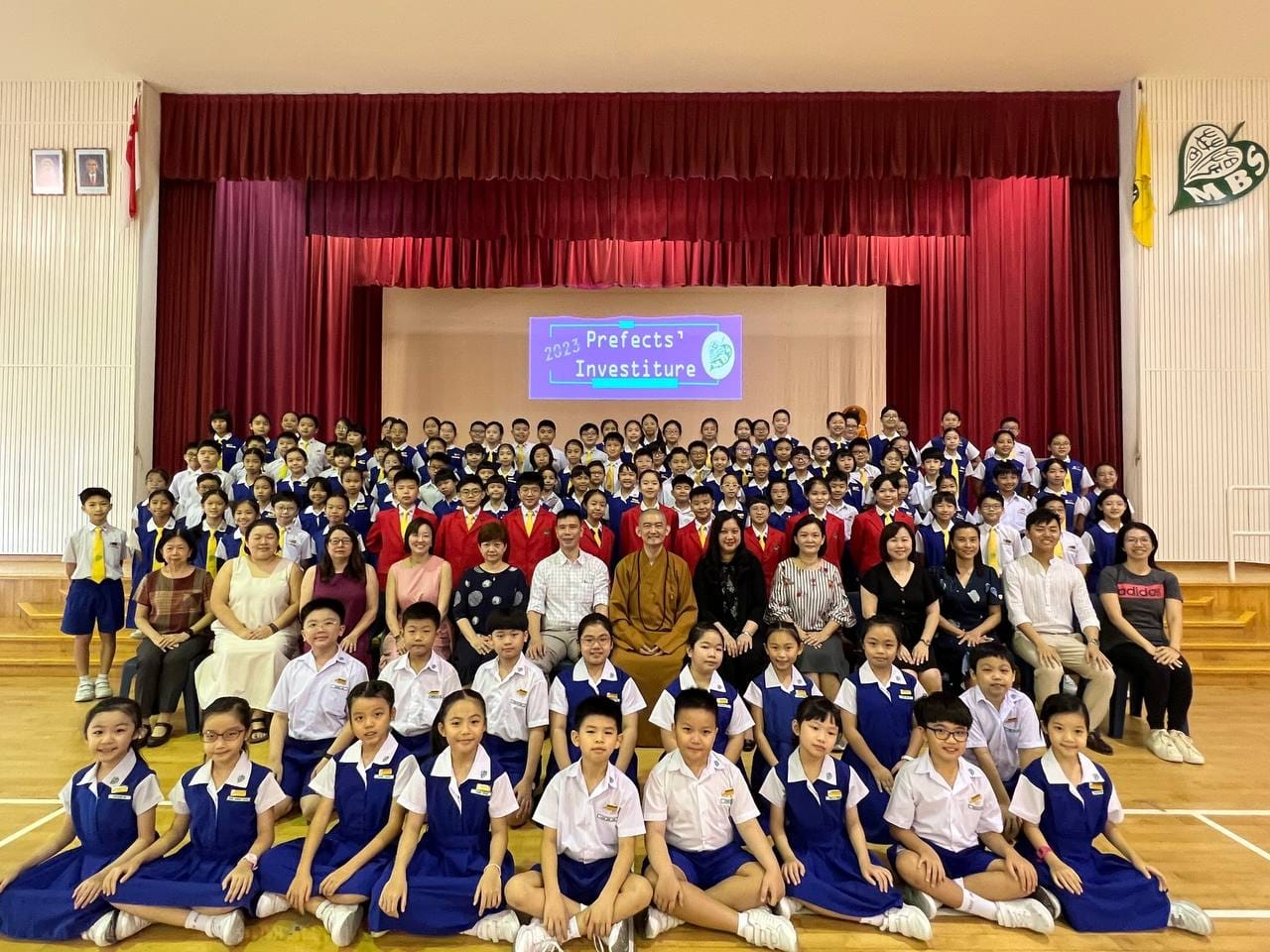 Group prefects taking photo with VIP and teachers posing in a school hall at the 2023 Prefects Investiture ceremony.